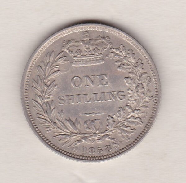 1858 silver shilling coin featuring Queen Victoria young head on the Obverse. The Reverse has a crown, laurel and oak leaves within an open wreath.