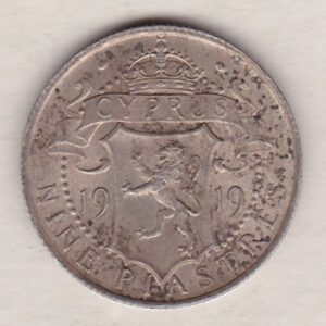 1919 Cyprus Nine Piastres coin. The obverse features King George V. The reverse features a crowned shield of arms which divides the dates.