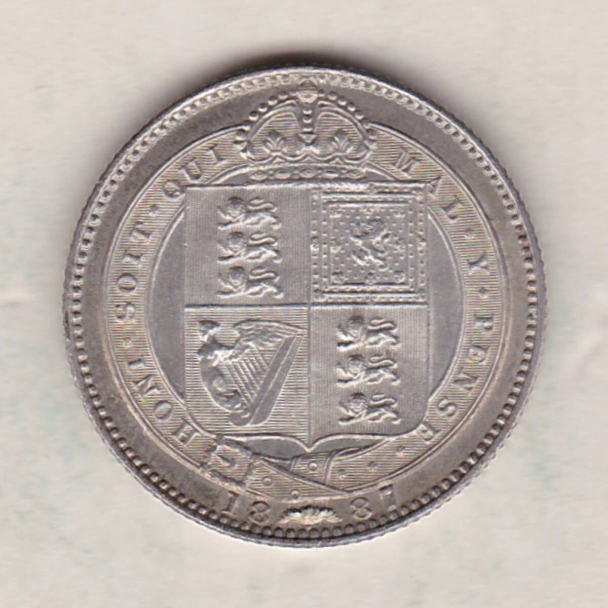 1887 Silver Shilling coin featuring Queen Victoria on the Obverse. The Reverse features the crowned Royal shield within Garter, with divided date below.
