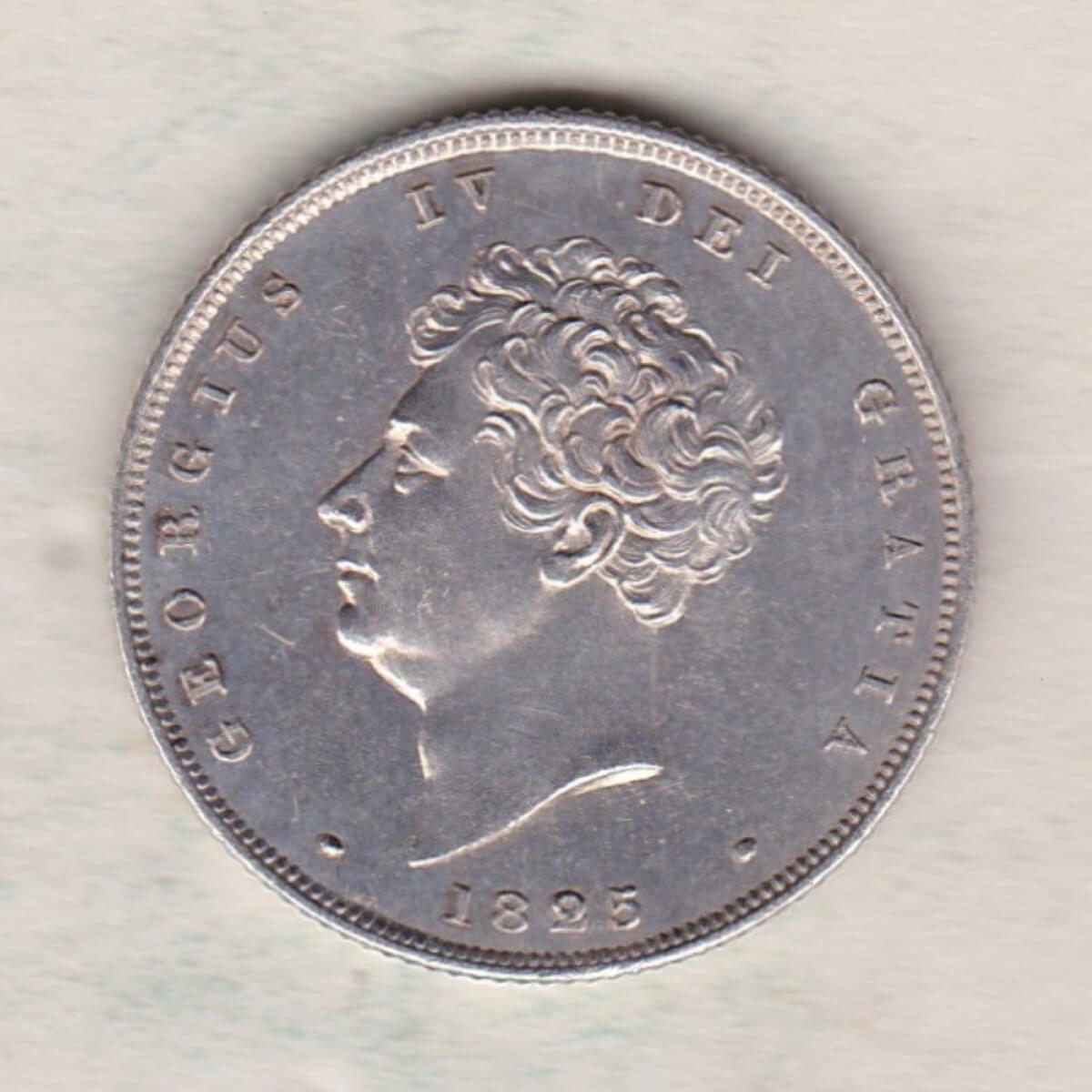 1825 silver shilling coin featuring King George IV on the Obverse. The Reverse has a crowned lion, legend around, national flower emblems below.