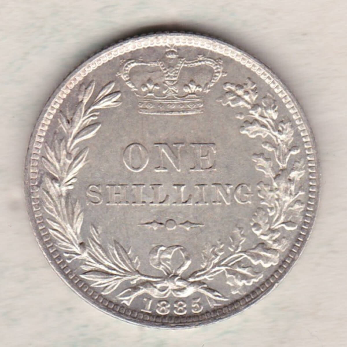 1885 silver shilling coin featuring Queen Victoria young head on the Obverse. The Reverse has a crown, laurel and oak leaves within an open wreath.