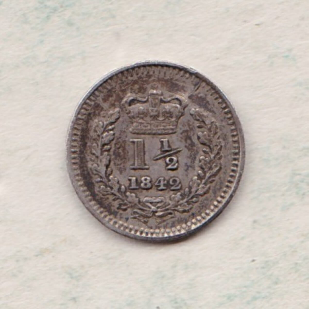 1842 Silver Three Halfpence coin features the portrait of Queen Victoria. The reverse has the crowned denomination above the date within an oak wreath.