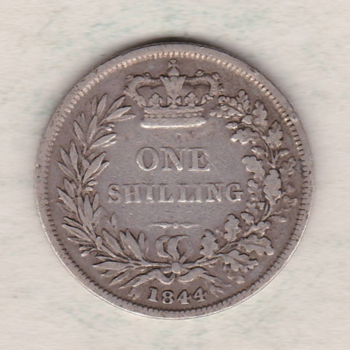1844 silver shilling coin featuring Queen Victoria young head on the Obverse. The Reverse has a crown, laurel and oak leaves within an open wreath.