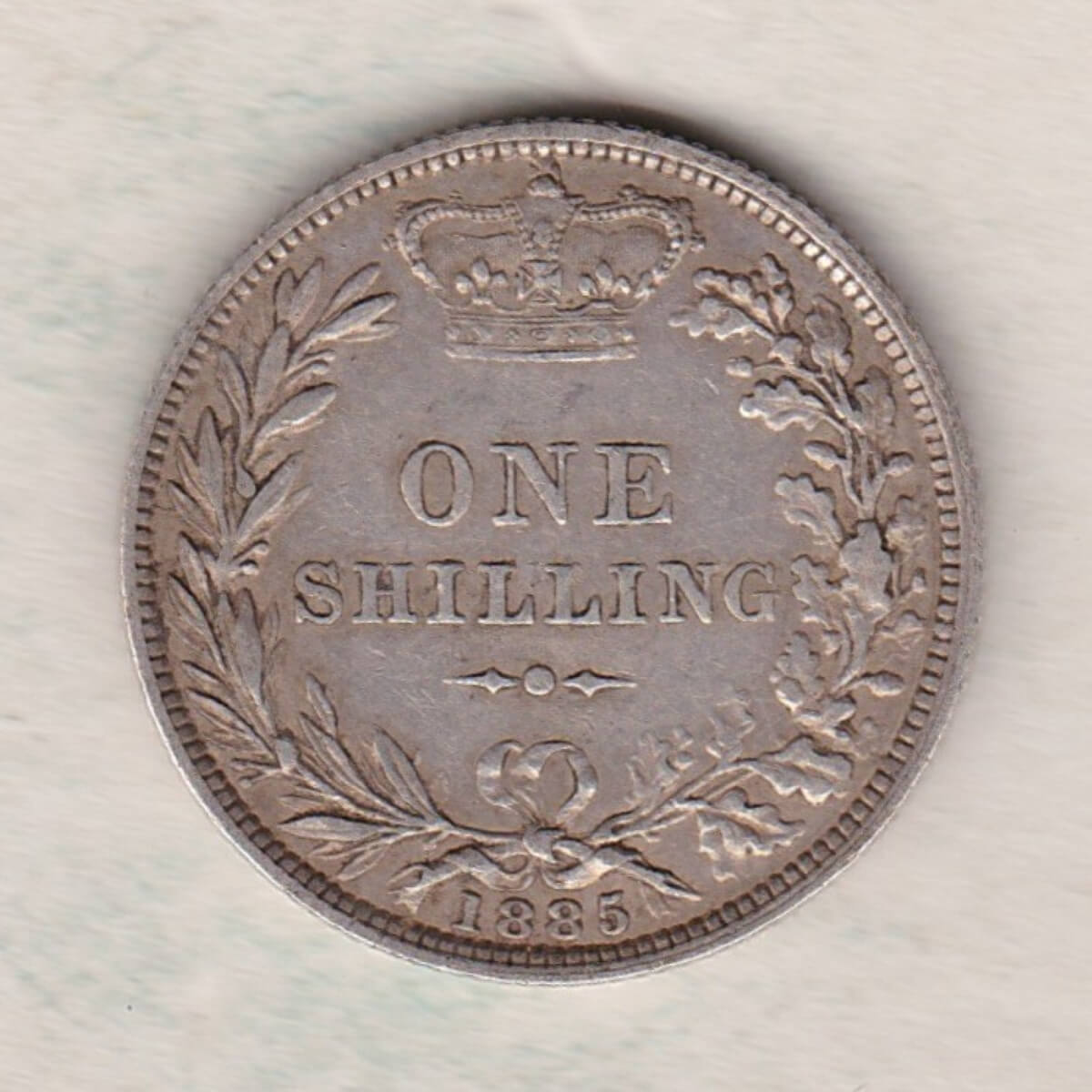1885 silver shilling coin featuring Queen Victoria young head on the Obverse. The Reverse has a crown, laurel and oak leaves within an open wreath.