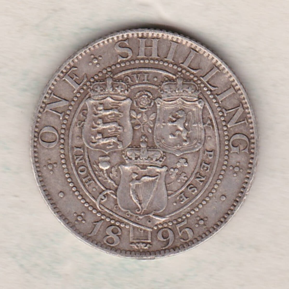 1895 Silver Shilling coin featuring Queen Victoria on the Obverse. The Reverse features the crowned shields of arms with national flower emblems between.